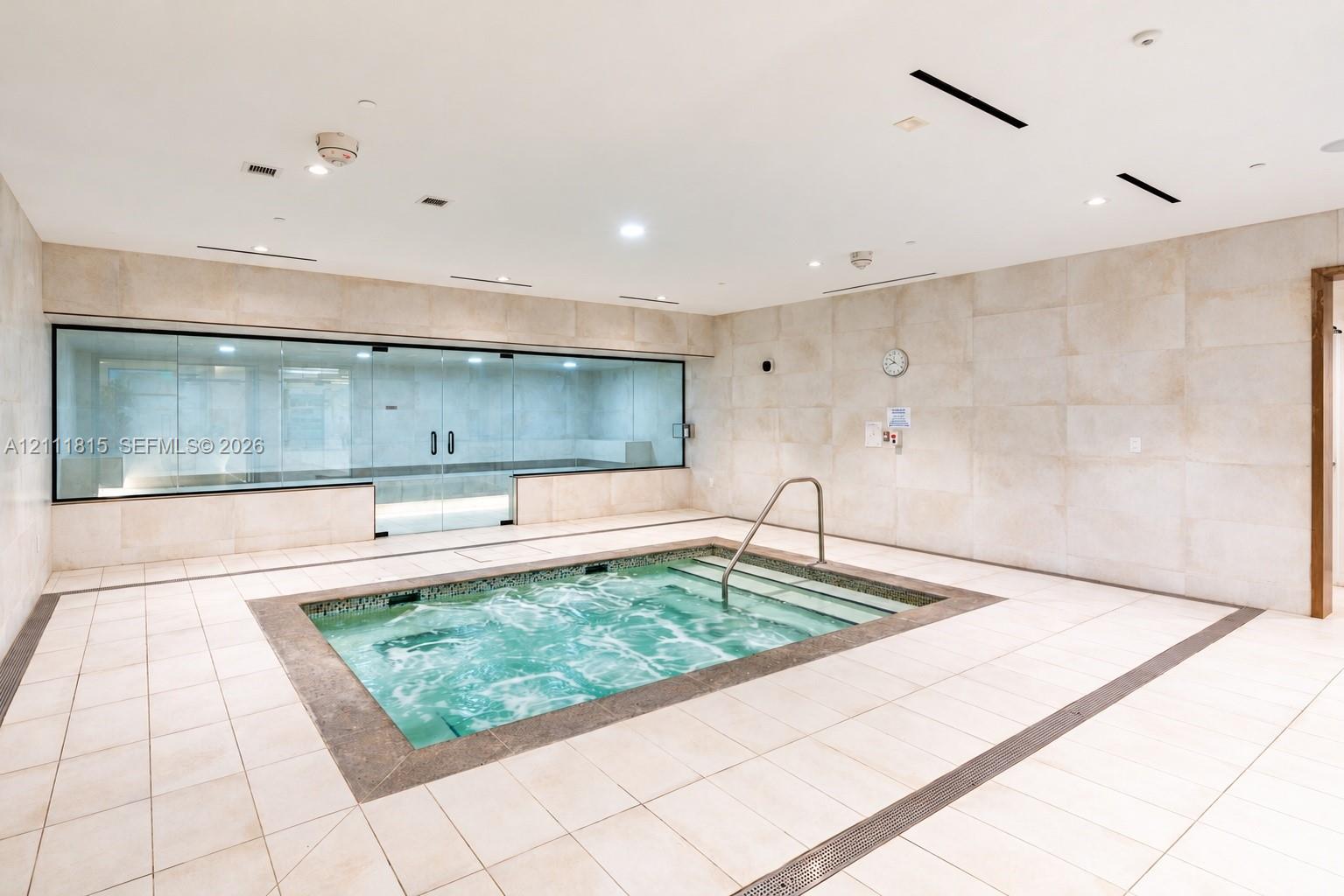 Indoor spa room featuring a tiled plunge pool, recessed lighting, expansive wall-to-wall glass enclosure, and stone-finish wall cladding Indoor spa room featuring a tiled plunge pool, recessed lighting, expansive wall-to-wall glass enclosure, and stone-finish wall cladding