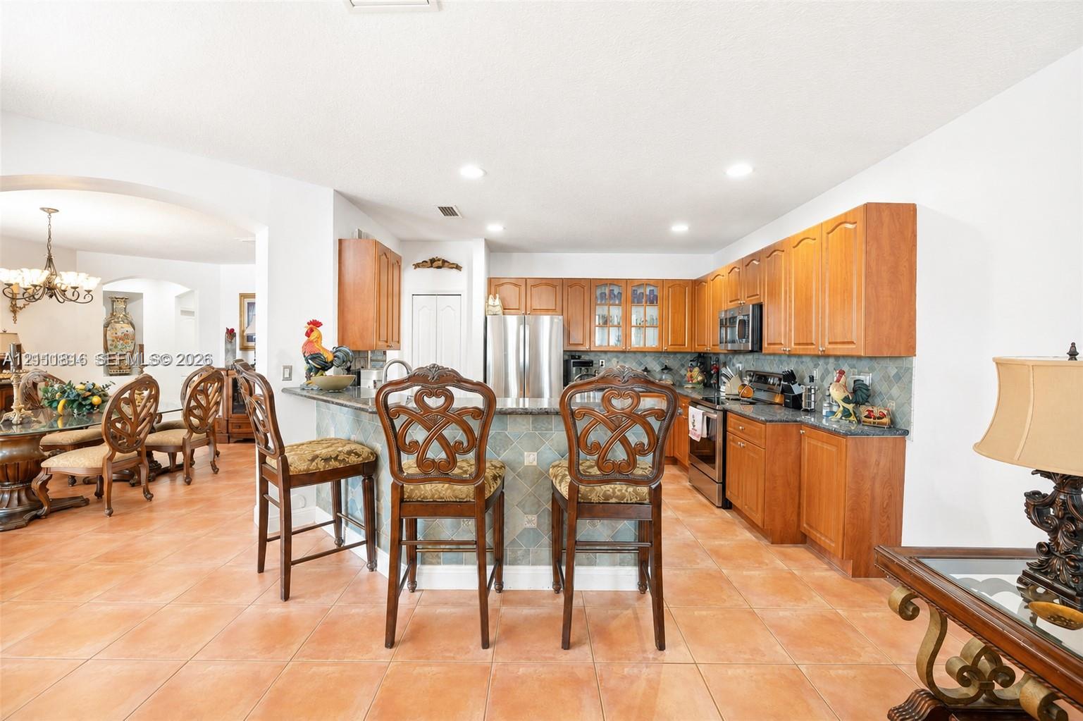Kitchen featuring wood cabinetry, stone countertops, stone tile backsplash, stainless steel appliances, and a peninsula with bar seating