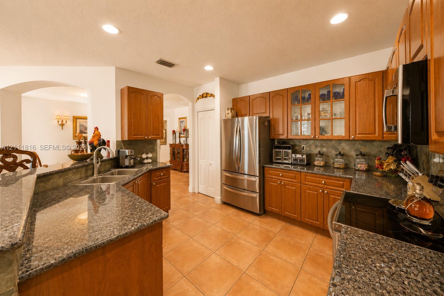 Kitchen featuring wood cabinetry, stone-surface countertops, tile flooring, stainless steel appliances, and glass-paneled upper cabinets