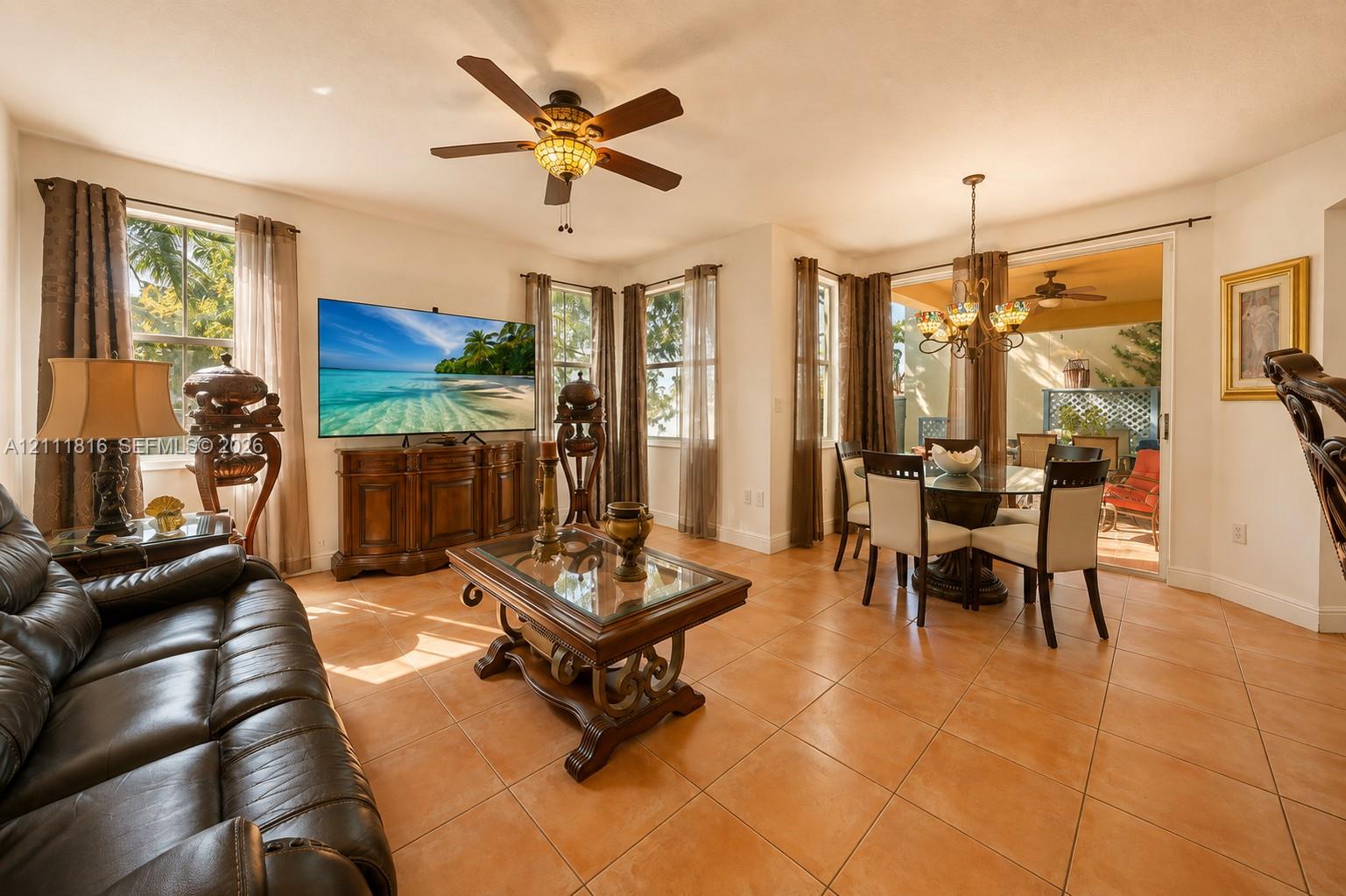 Open-concept living space featuring large-format tile flooring, a multi-blade ceiling fan with integrated lighting, and a multi-arm chandelier