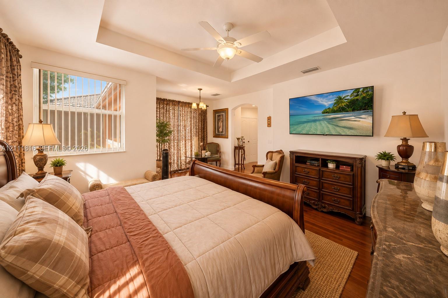 Bedroom featuring a tray ceiling, recessed lighting, ceiling fan, wood-finish flooring, and arched entryway