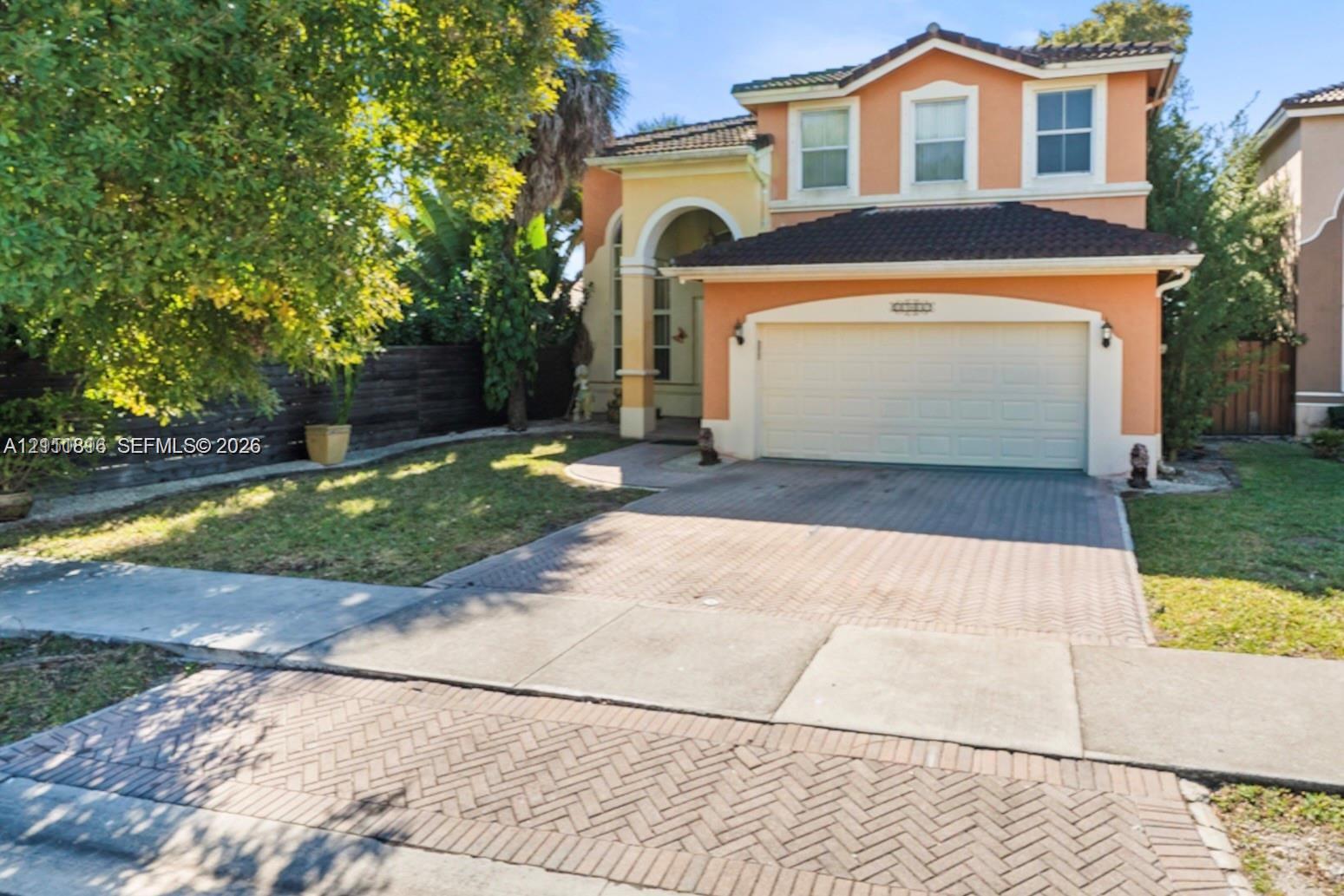 Two-story residence featuring a tile roof, paver driveway, arched entryway, and attached two-car garage