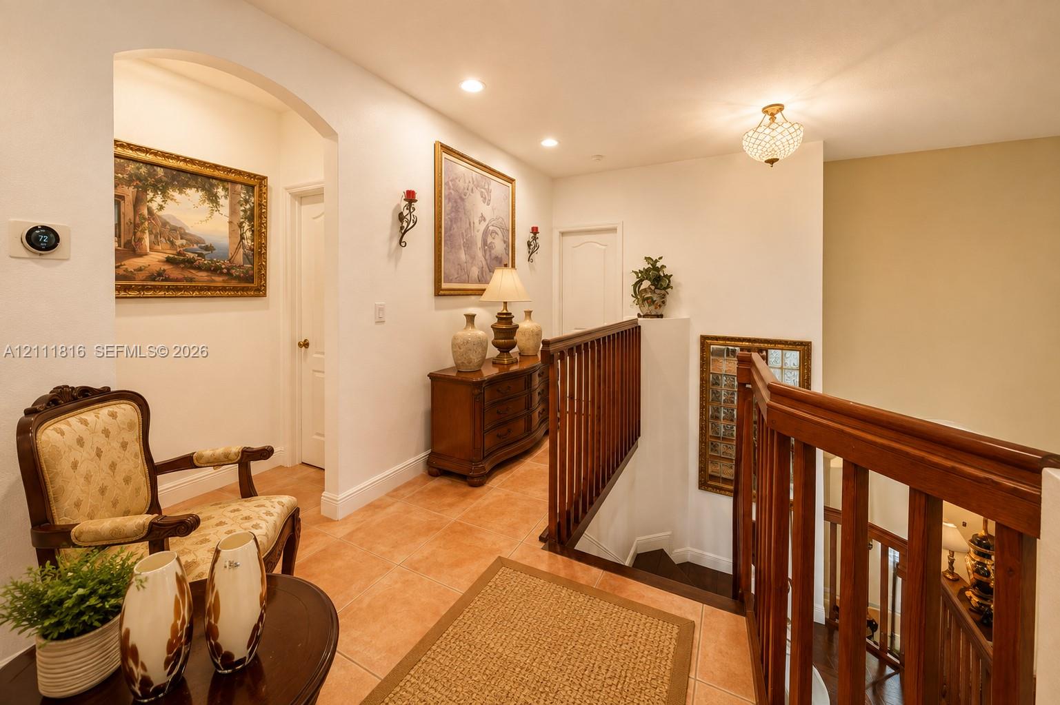 Hallway featuring arched architectural detailing, ceramic tile flooring, a wood-slat banister, and recessed lighting