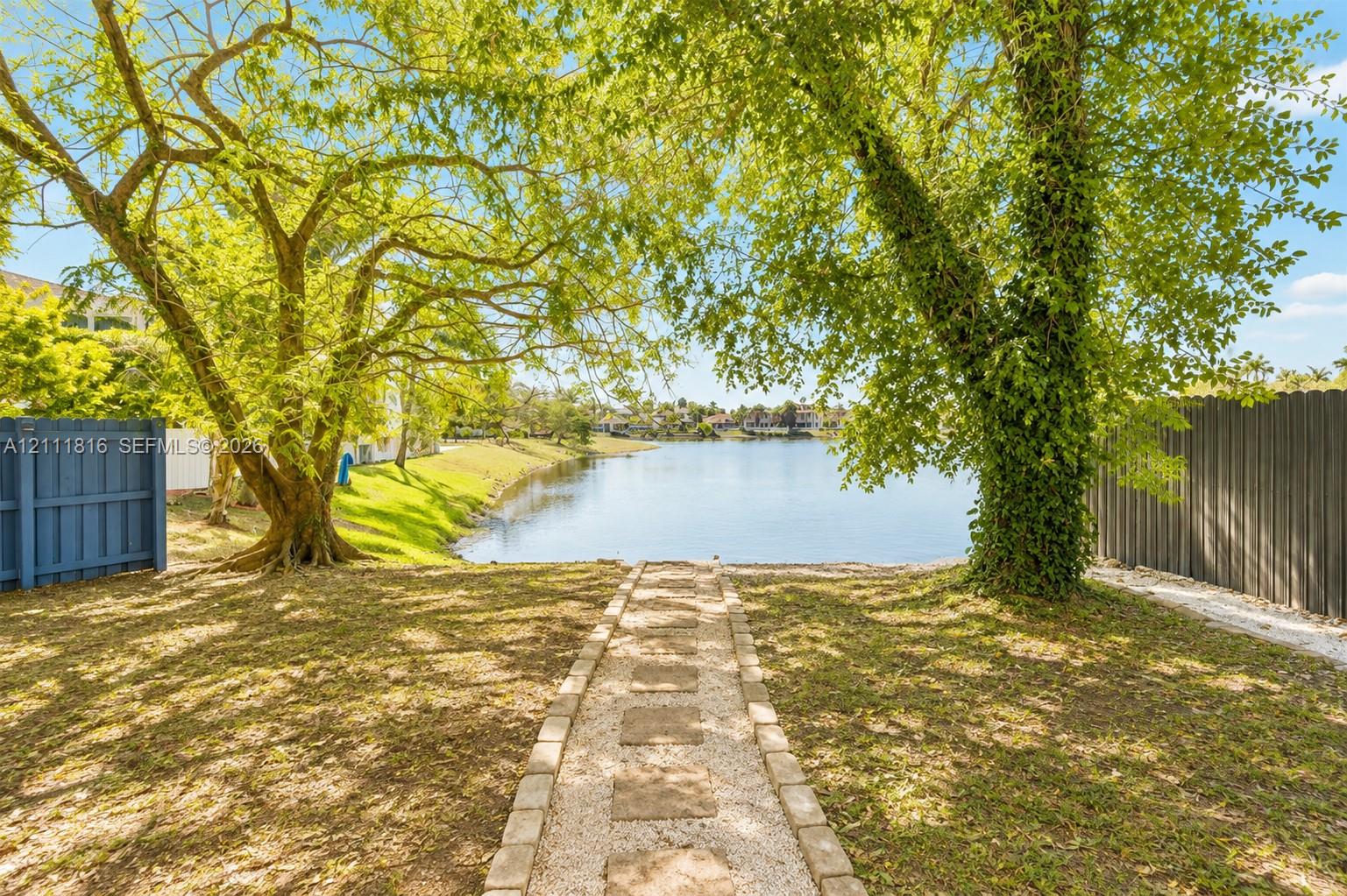 Waterfront lot featuring a stone-paver walkway, mature trees, and privacy fencing
