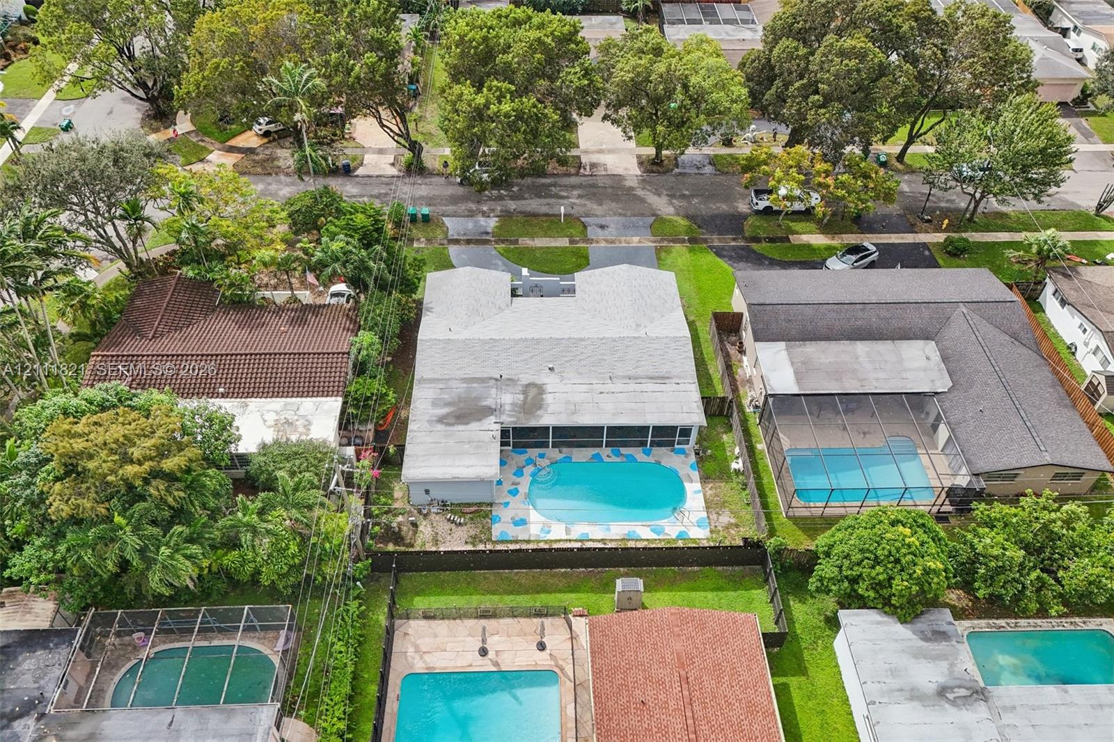 Aerial perspective of a property featuring an in-ground swimming pool, a screened-in patio, and mature landscaping