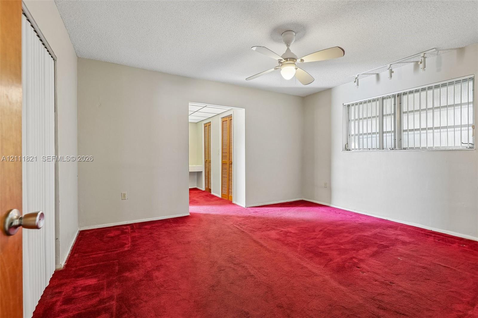 Red carpeting, white ceiling fan with integrated lighting, track lighting, and louvered closet doors