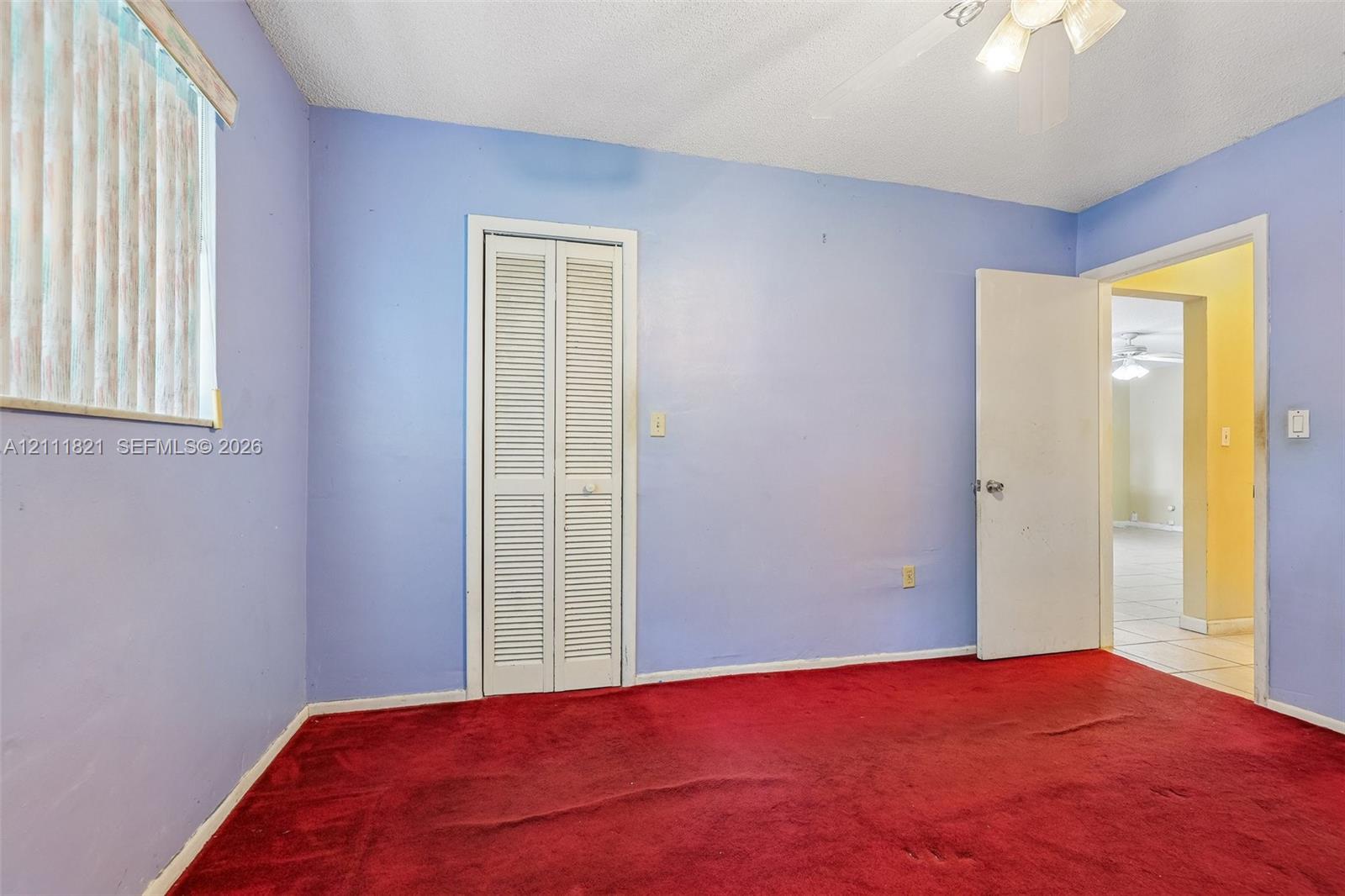 Interior room featuring a ceiling-mounted light fixture, carpeted flooring, a closet with bi-fold louvered doors, and a vertical window blind
