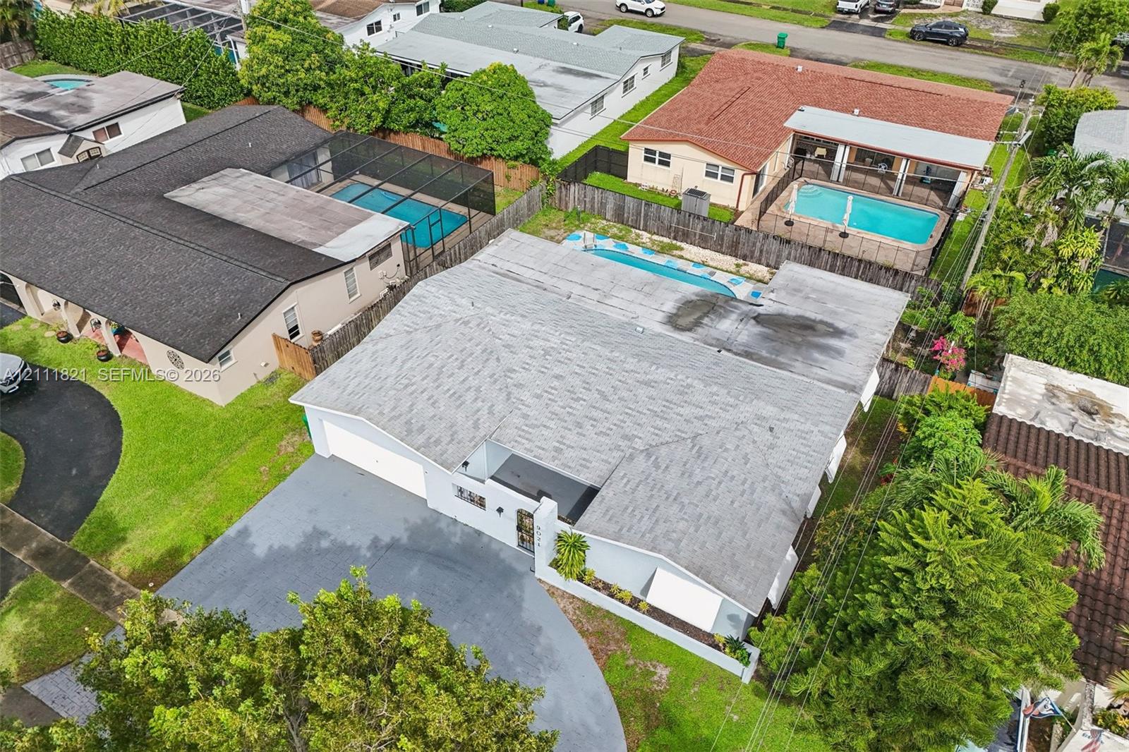 Aerial perspective of a single-story residence featuring a shingled roof, a paved driveway, and an in-ground swimming pool