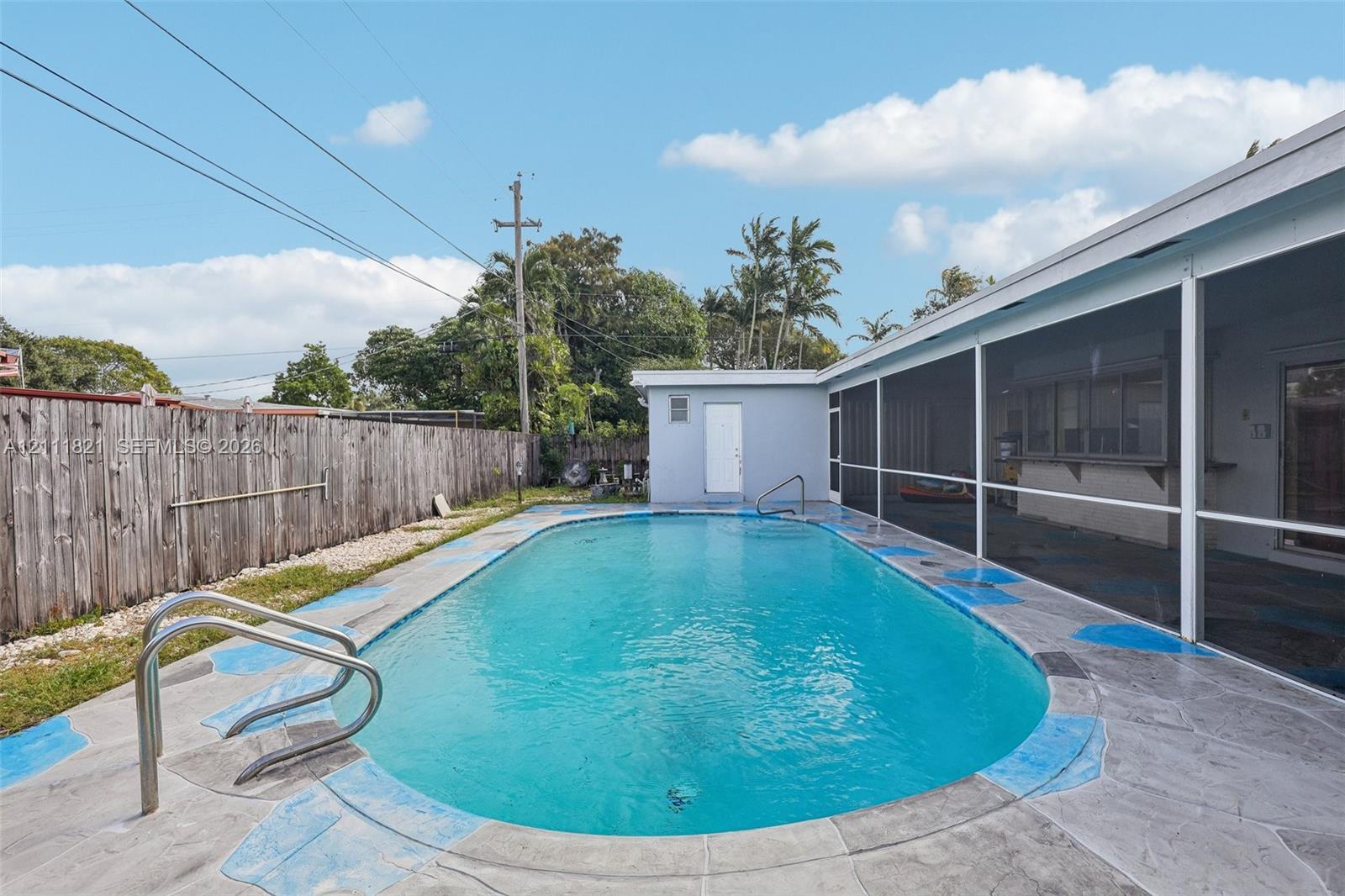 In-ground swimming pool with a metal handrail, surrounded by a concrete pool deck and an attached screen enclosure