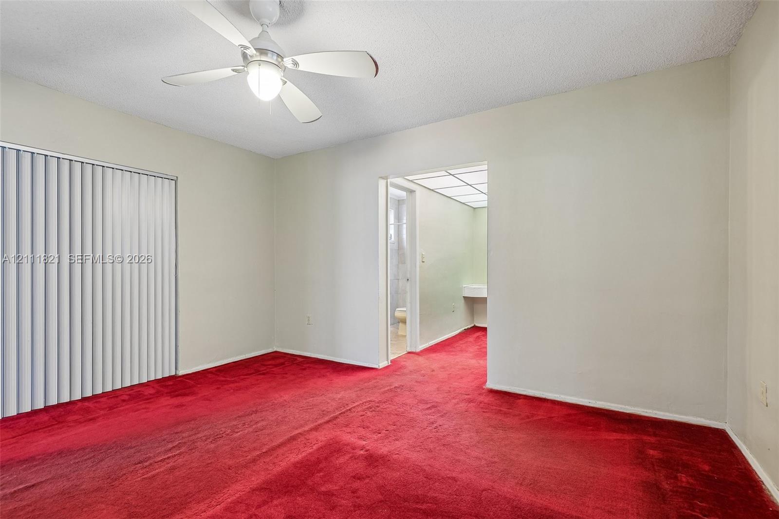 Interior room featuring red wall-to-wall carpeting, ceiling fan with integrated lighting, and vertical window blinds