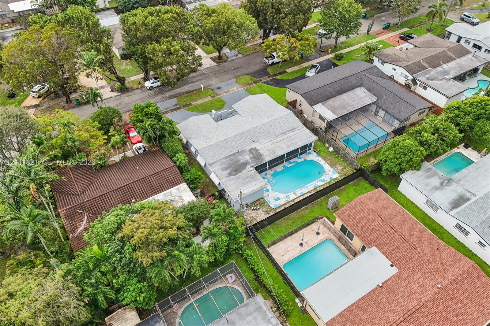 Aerial perspective of a single-story residence featuring a shingled roof, a screened-in pool enclosure, and a concrete patio