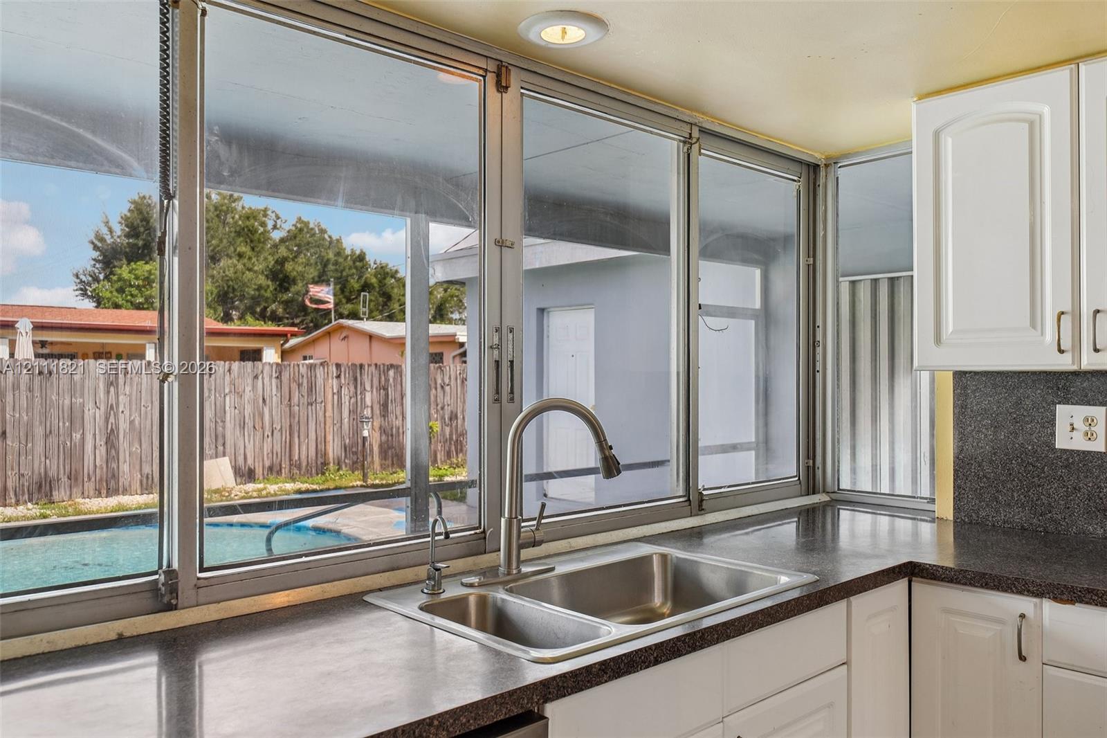 Kitchen sink featuring a dual-basin stainless steel basin, high-arc faucet, solid-surface countertops, white cabinetry, and multi-pane window configuration