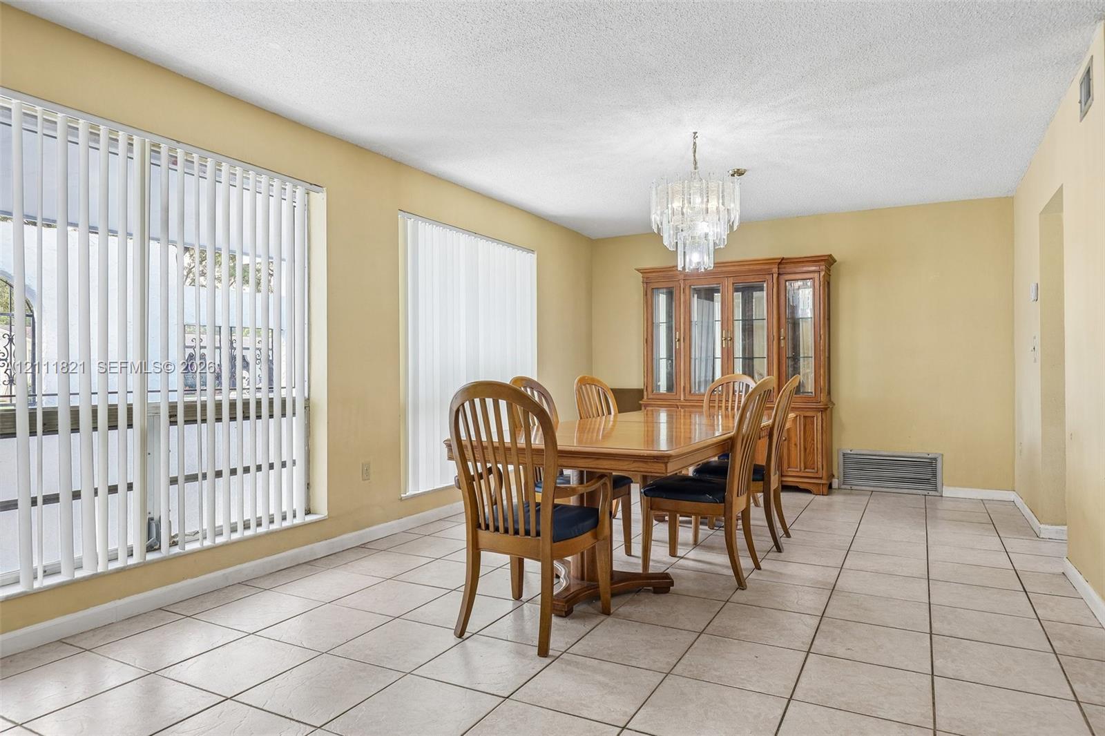 Ceramic tile flooring, built-in wooden cabinetry, crystal chandelier lighting, and large windows with vertical blinds