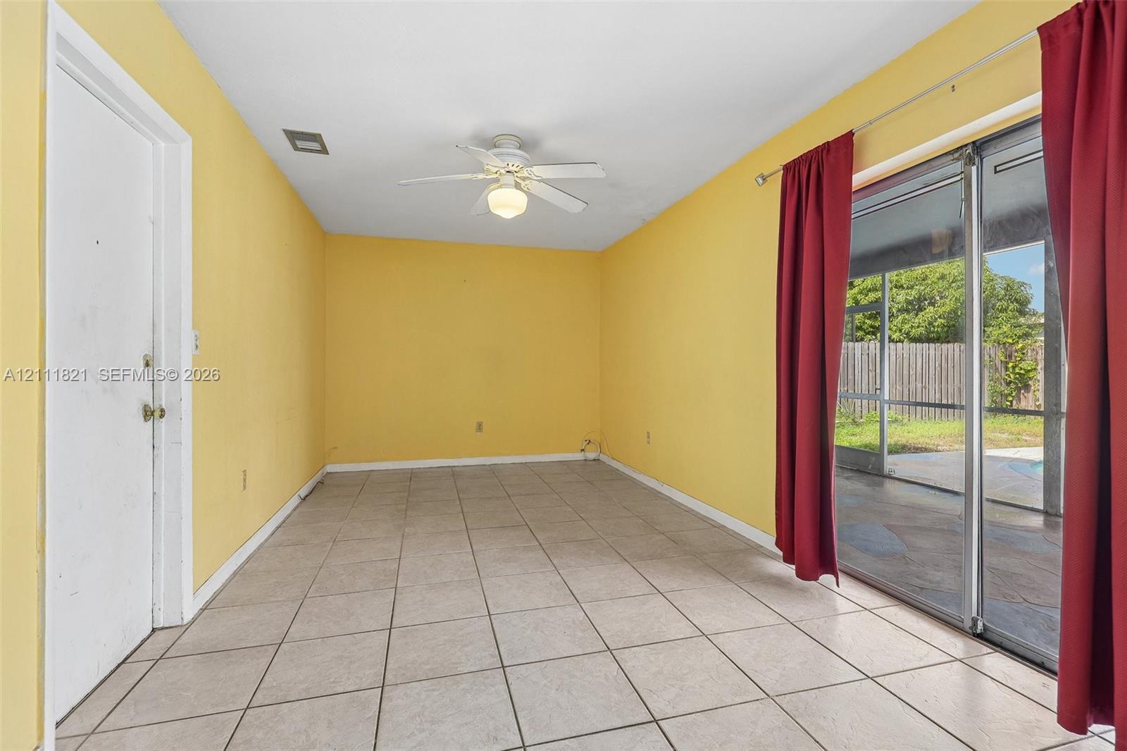 Interior room featuring neutral tile flooring, a central ceiling fan with an integrated light fixture, and a sliding glass door providing external access