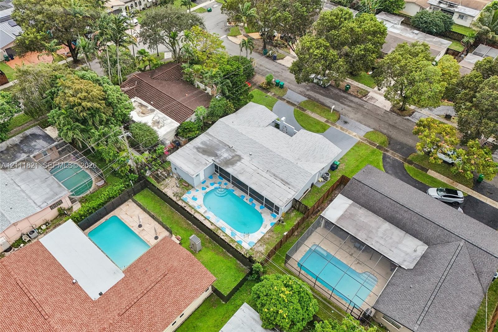 Aerial perspective featuring a shingled roof, an in-ground swimming pool, a screened-in lanai, and a fenced-in grass backyard