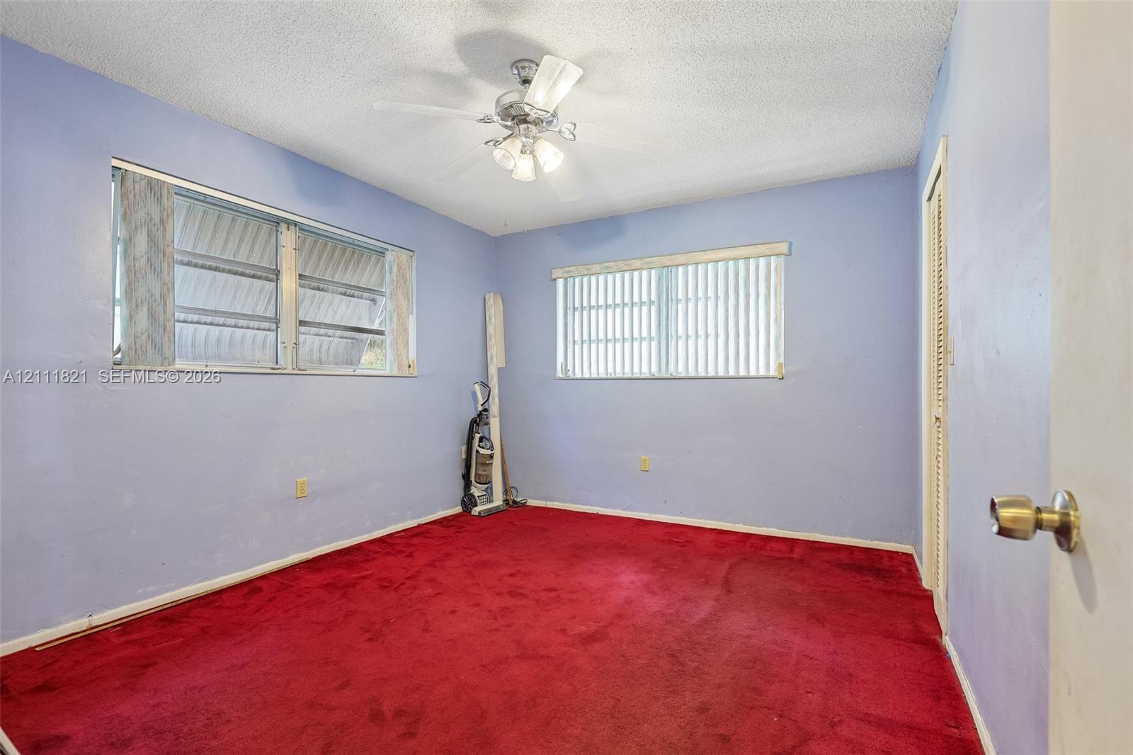 Room featuring wall-to-wall carpeting, dual windows with blinds, a multi-light ceiling fan, and a louvered closet door