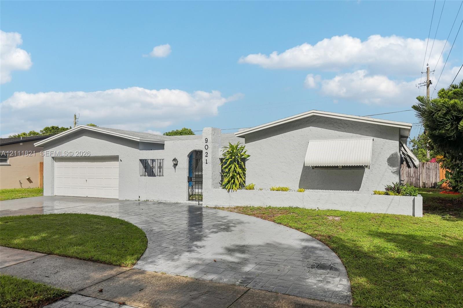 Single-story residence featuring a gray stucco exterior, arched entry, stamped concrete driveway, attached garage, and fixed window awnings