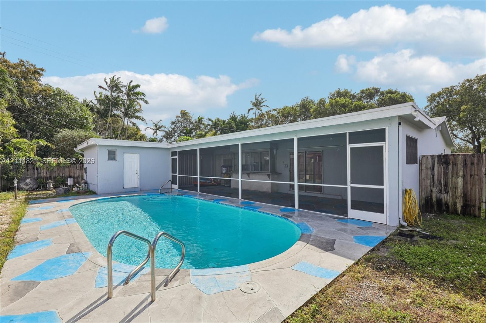 In-ground swimming pool with metal handrail, screened-in lanai, and flagstone-style pool deck