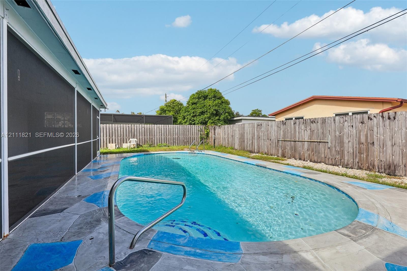 Oval-shaped swimming pool with a metal handrail and paved deck, enclosed by a screened-in structure and wood privacy fencing