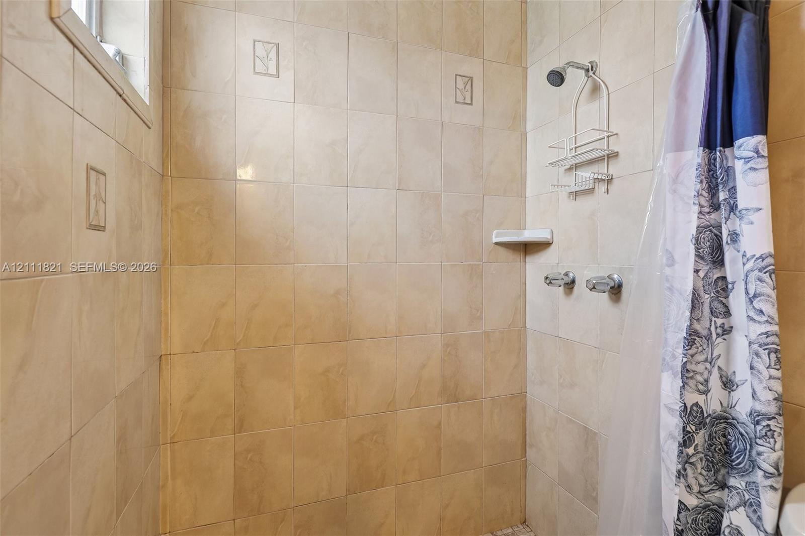 Shower enclosure featuring full-height neutral ceramic wall tiling, decorative accent tiles, a built-in recessed soap dish, and wall-mounted plumbing fixtures