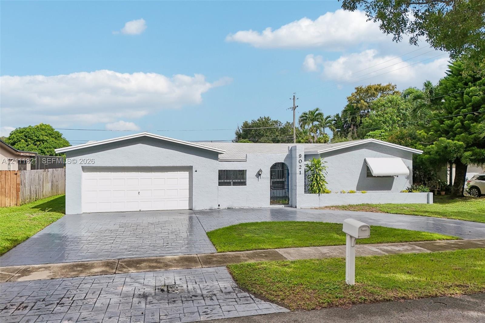 Single-story exterior featuring a light-toned masonry facade, a multi-car stamped concrete driveway, an attached garage, and a covered arched entryway