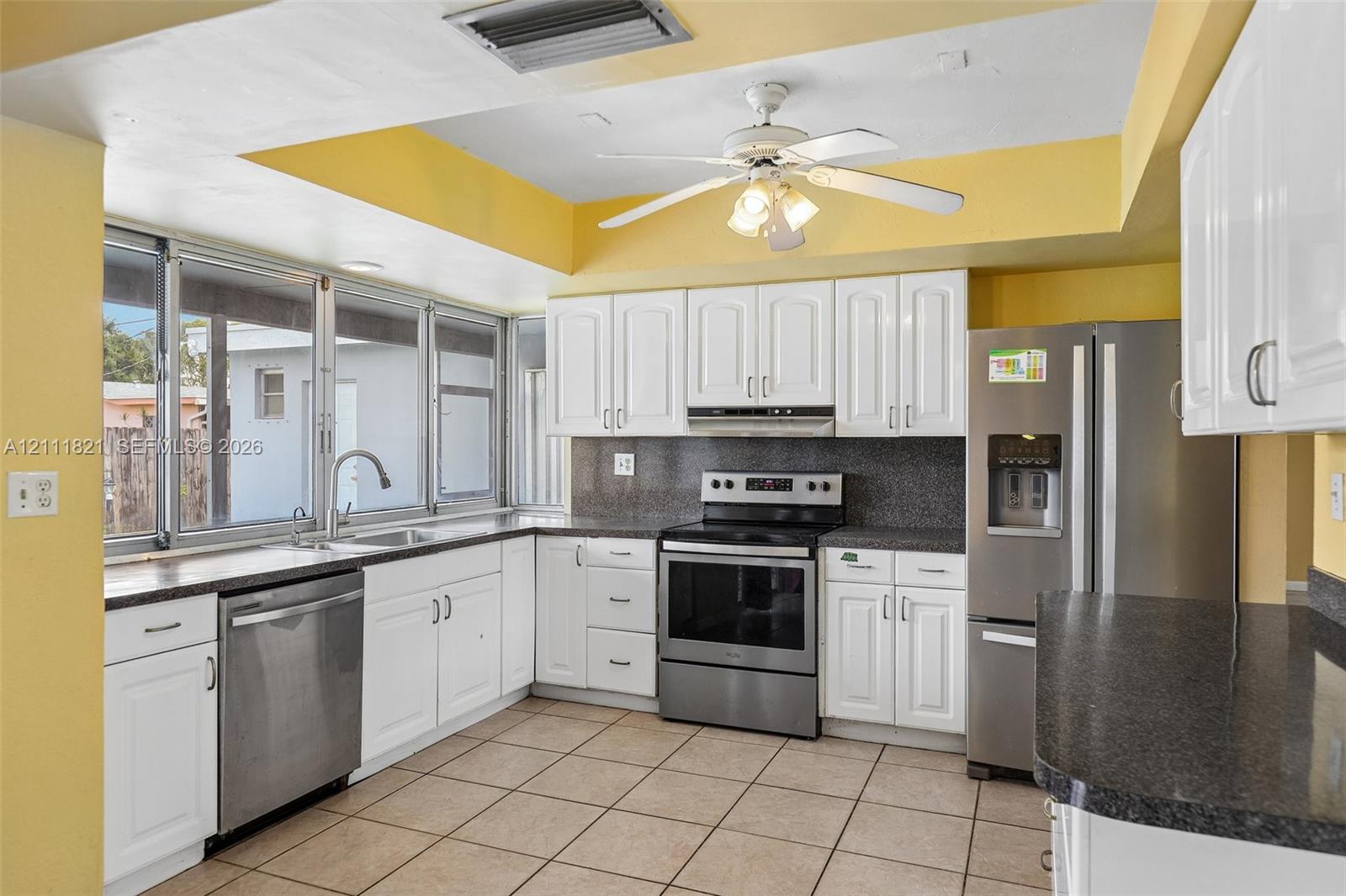 Kitchen featuring white shaker-style cabinetry, dark stone-finish countertops, tile flooring, and stainless steel appliances including a range, dishwasher, and refrigerator