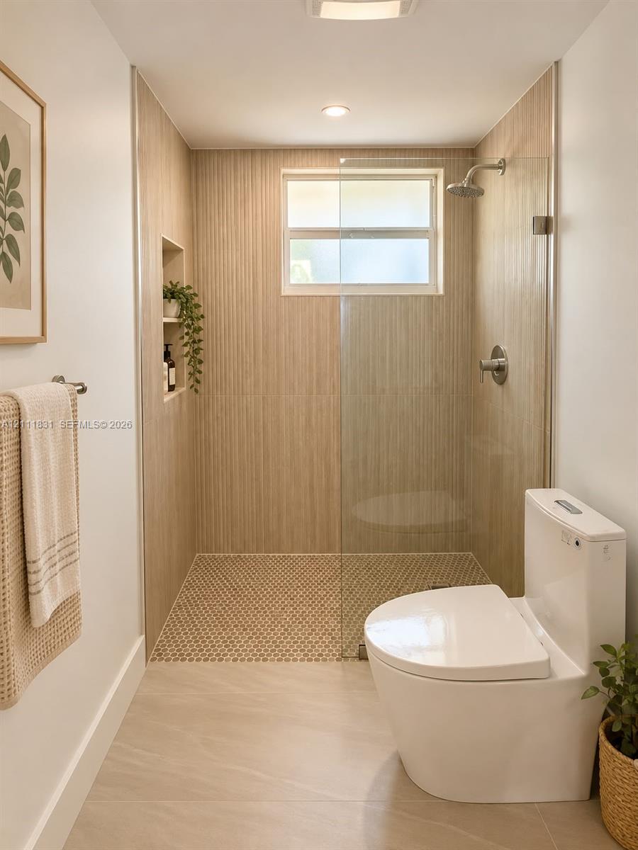 Walk-in shower with floor-to-ceiling textured tile, integrated recessed shelving, frameless glass enclosure, penny-round mosaic tile shower floor, and a wall-mounted shower head