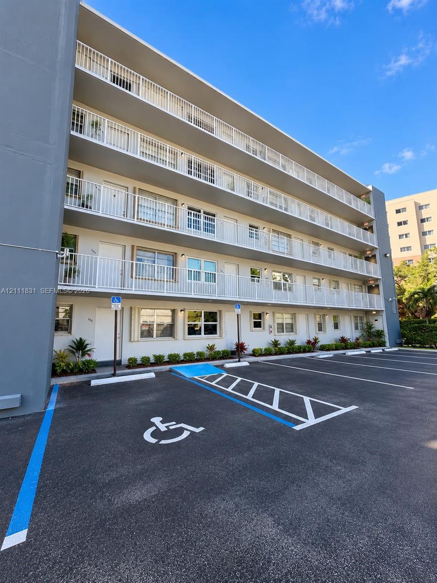 Multi-story exterior featuring white railed balconies, paved surface parking, and ground-level landscaping