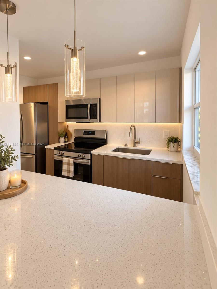 Kitchen featuring two-tone cabinetry with flat-panel doors, expansive stone-finish countertops, stainless steel appliances, under-cabinet lighting, and cylindrical pendant fixtures