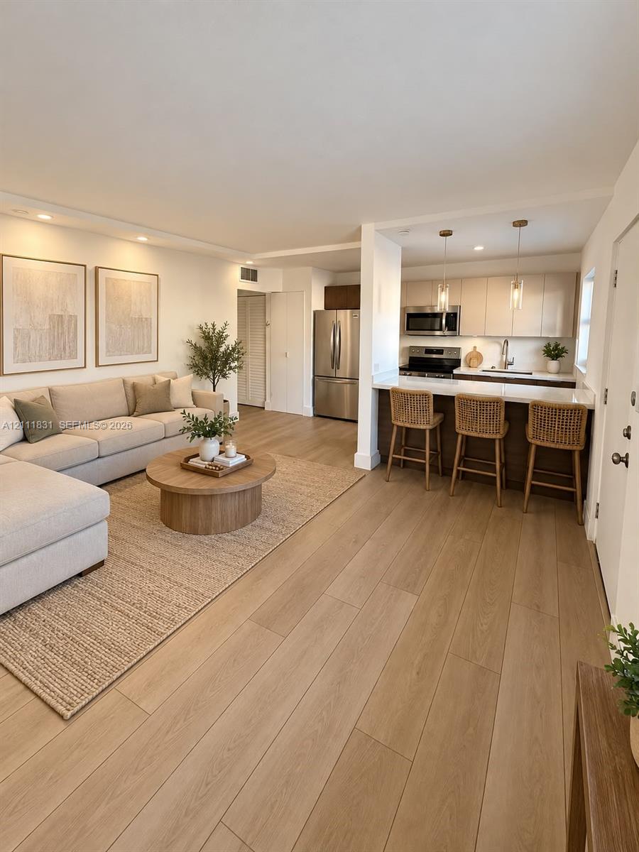 Open-concept interior featuring light wood-finish flooring, recessed lighting, and a kitchen with stainless steel appliances, flat-panel cabinetry, and a breakfast bar