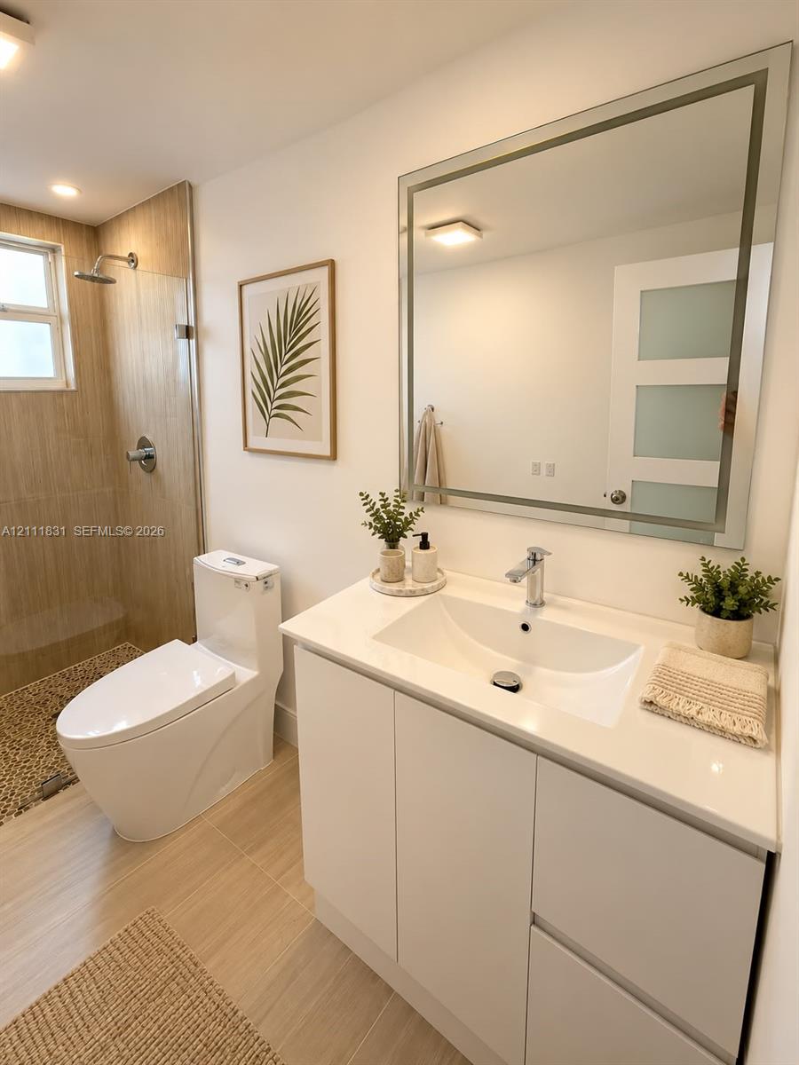 White vanity cabinet with an integrated sink and light-toned countertop, framed mirror, walk-in shower with tile surround, and neutral floor tiling