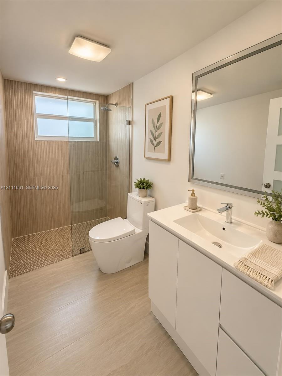Bathroom featuring a walk-in shower with vertical tile surround and a glass partition, vanity with a white countertop and integrated sink, dual-flush toilet, and a framed mirror