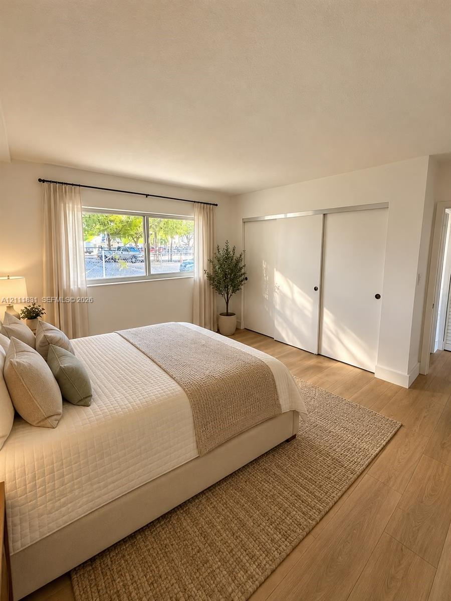 Neutral interior space featuring wood-finish flooring, a large horizontal window with a black metal rod, and built-in sliding closet doors