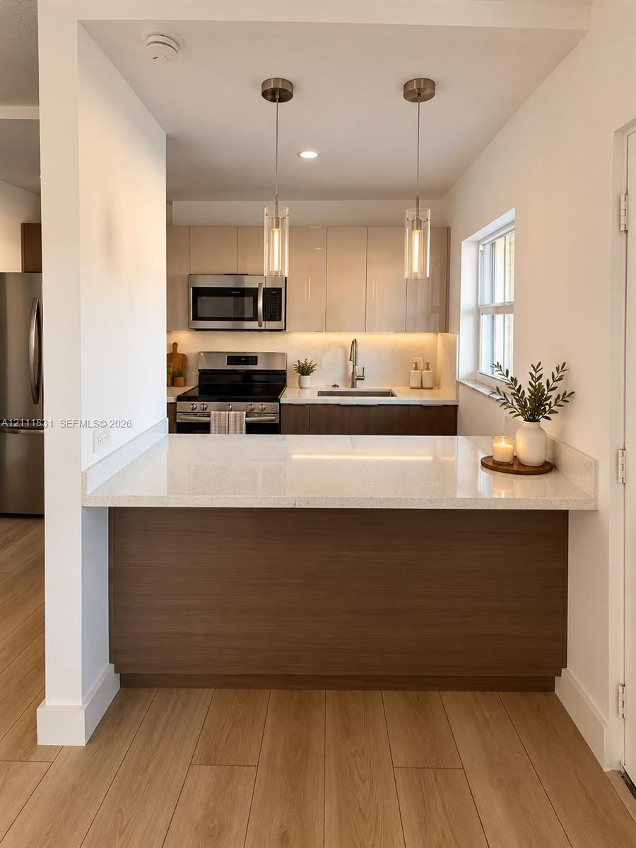 Kitchen featuring quartz countertops, two-tone cabinetry, stainless steel appliances, wood-finish flooring, and dual glass pendant lights