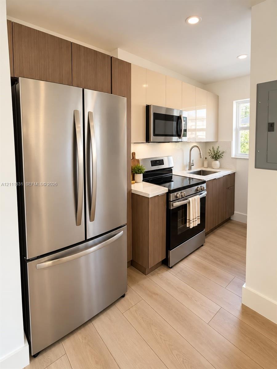 Kitchen featuring two-tone cabinetry with wood-finish lower units and high-gloss upper cabinets, stainless steel appliances, stone-surface countertops, and wood-finish flooring