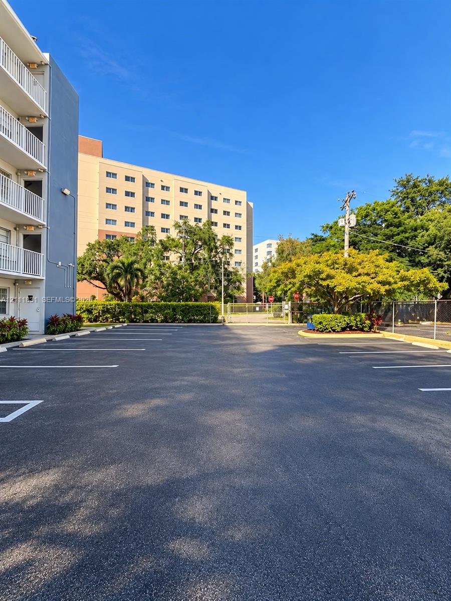 Paved surface parking area featuring marked spaces, perimeter metal fencing, and mature landscaping