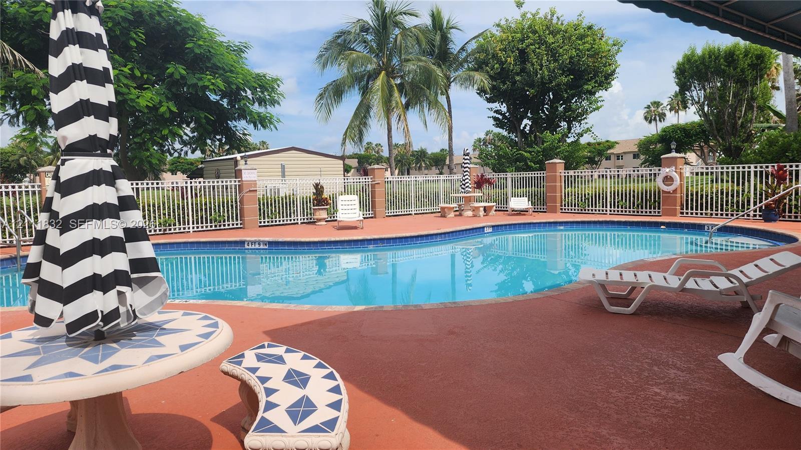 In-ground swimming pool featuring a curved design, masonry perimeter fencing with pillar accents, and a textured deck surface