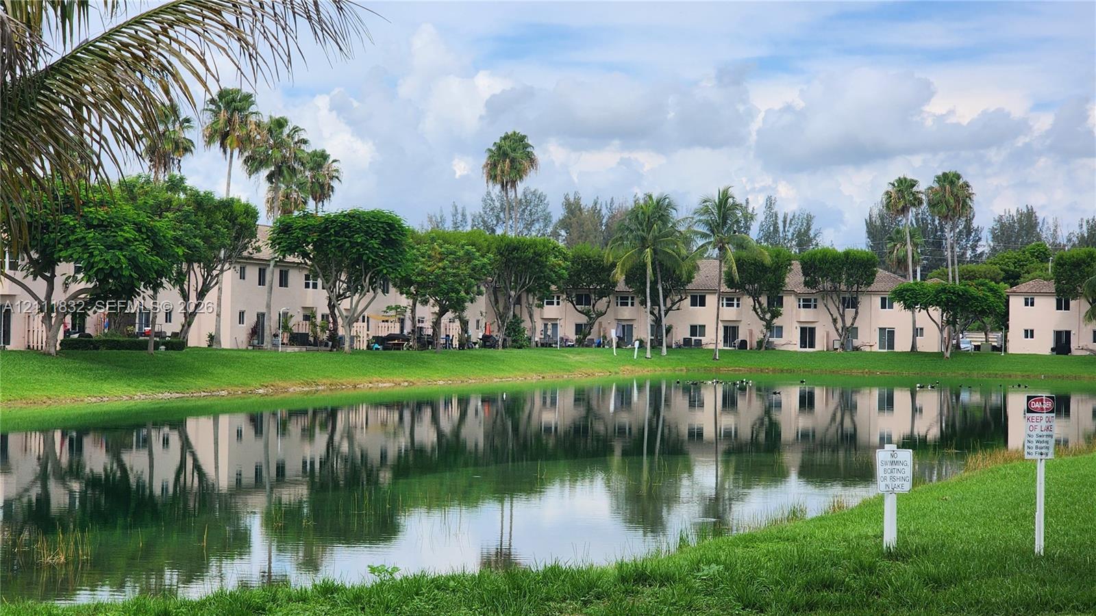 Waterfront exterior featuring a central pond, manicured lawn, and established palm trees