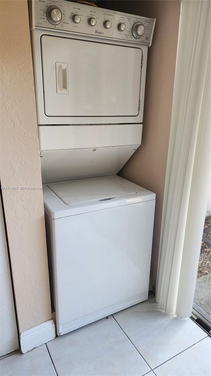 White stacked laundry unit featuring a top-load washer and a control panel with tactile rotary dials, installed within a tiled-floor alcove