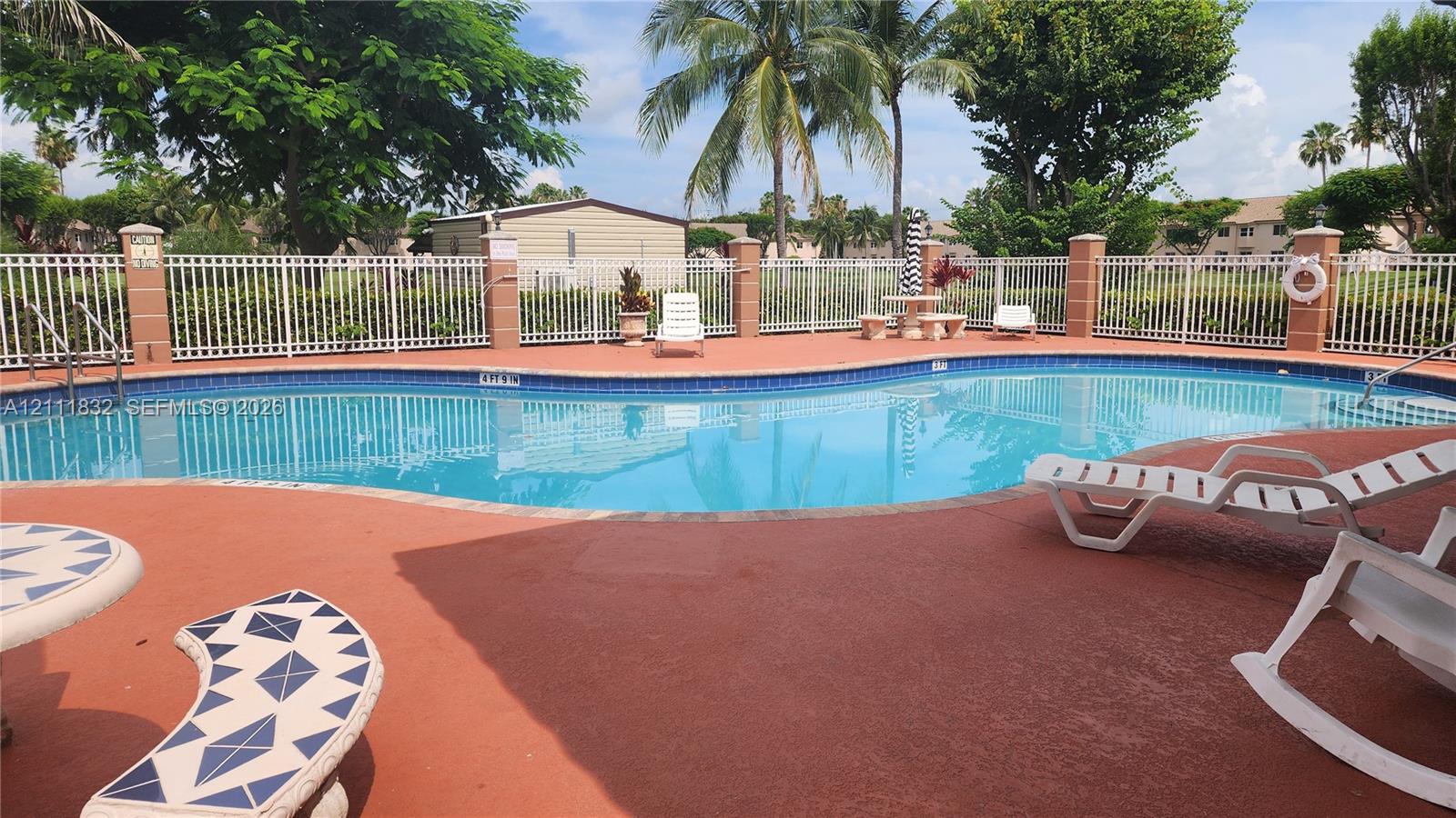 In-ground pool with tile coping, terracotta-toned concrete decking, and white metal perimeter fencing