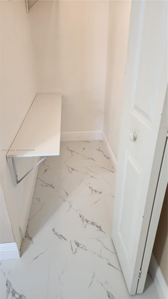 Storage area featuring large-format tile flooring with a veined pattern, a built-in wall-mounted shelf, and a bi-fold door
