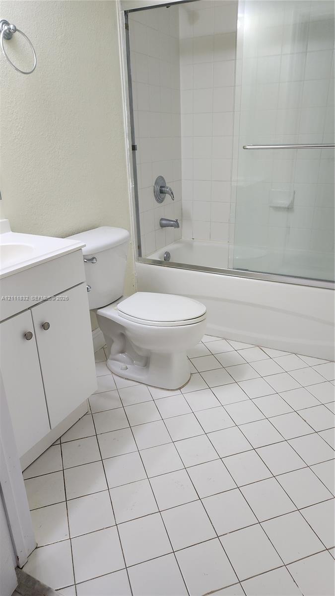 Bathroom featuring a white vanity cabinet, a shower and tub combination with a glass sliding enclosure, ceramic tile flooring, and a wall-mounted ring towel holder