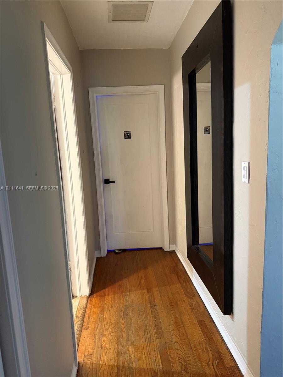 Hallway featuring wood-finish flooring, white panel door with matte black hardware, and wall-mounted dark-toned frame