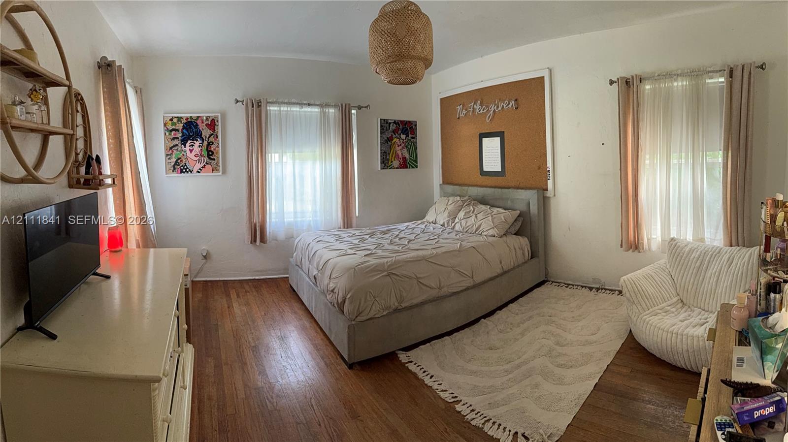 Bedroom featuring wood-finish flooring, two windows with adjustable window treatments, and a hanging woven light fixture