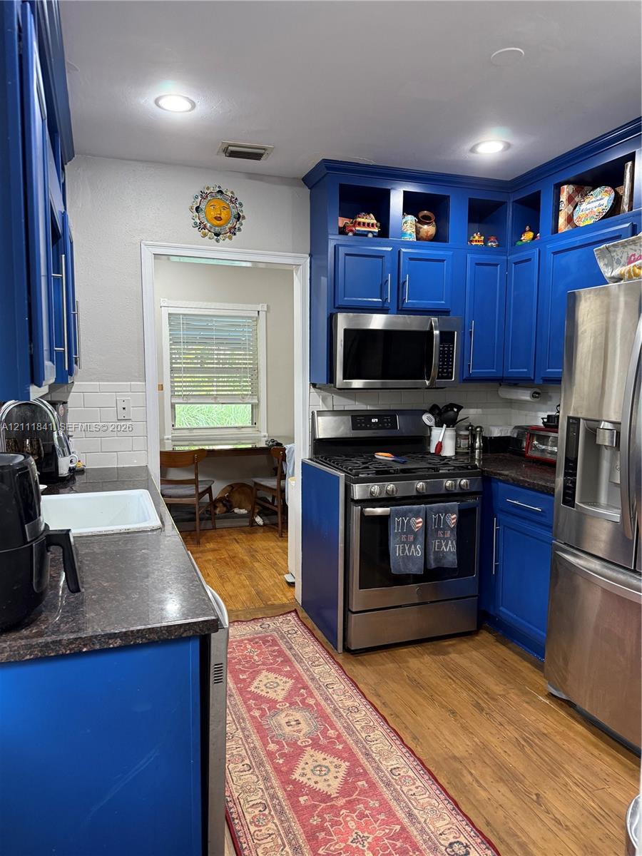 Kitchen featuring custom blue cabinetry, stone-finish countertops, white subway tile backsplash, recessed lighting, and stainless steel appliances