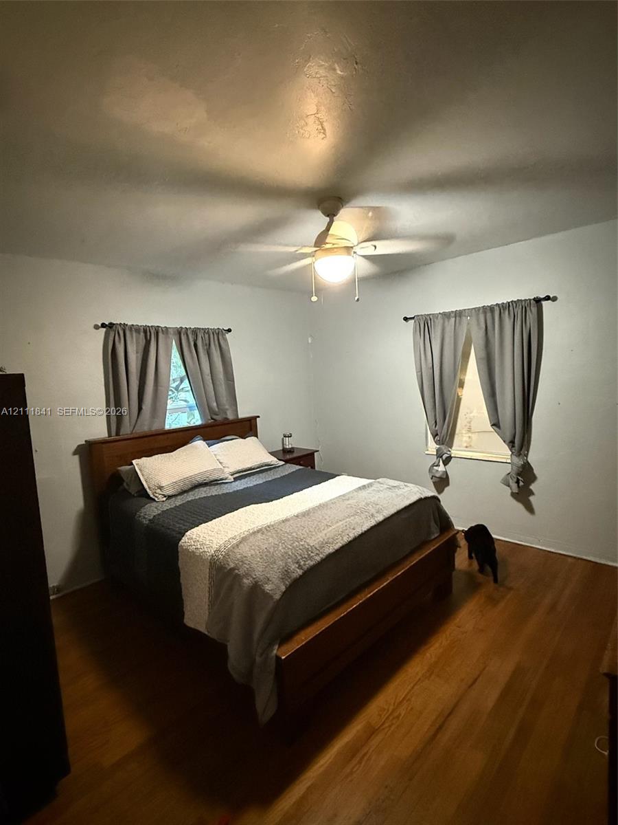 Room featuring wood-finish flooring, two windows with curtain rods, and a ceiling fan with integrated lighting