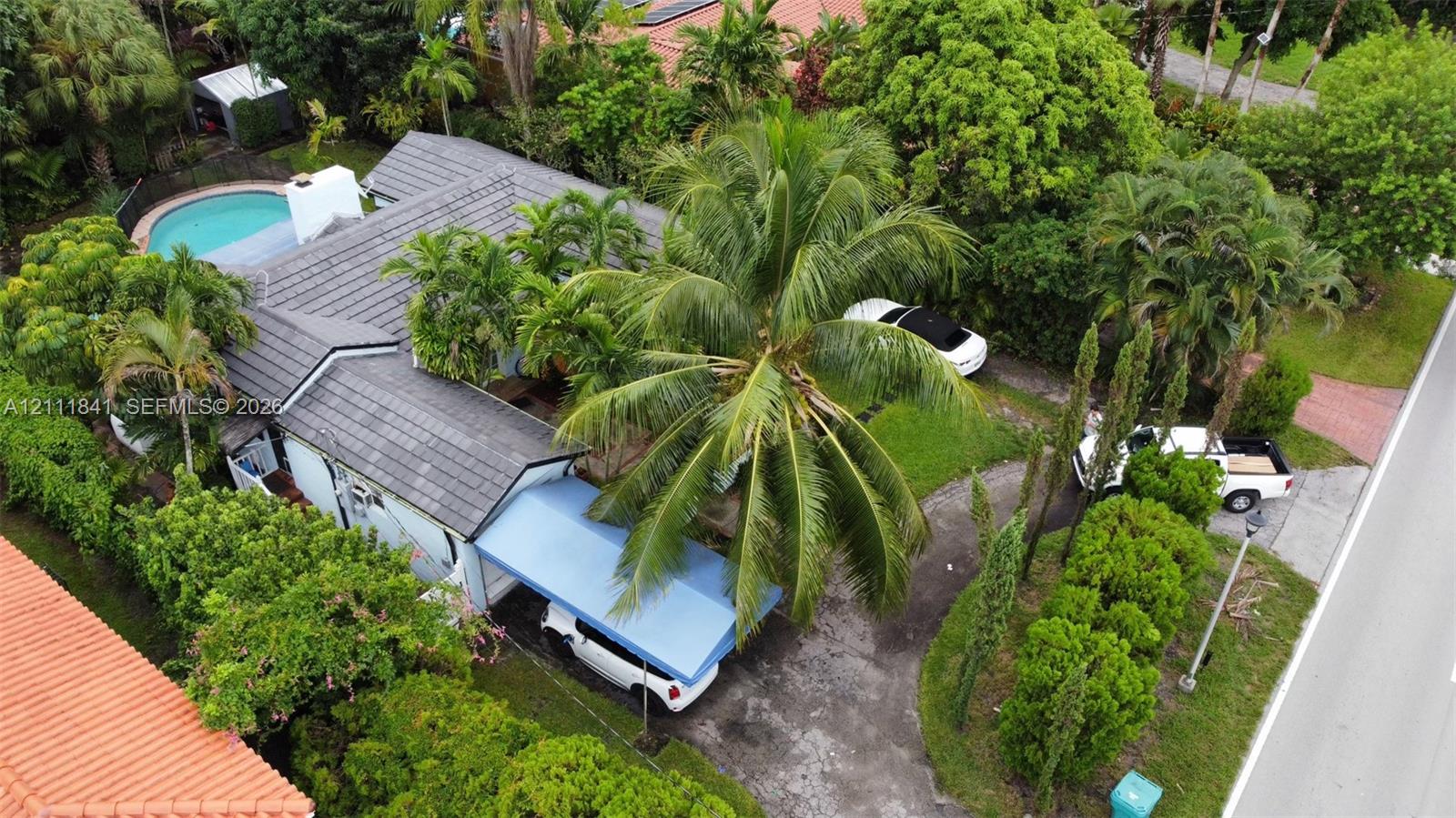 Aerial perspective of a property featuring a tile roof, an outdoor swimming pool, a covered carport, and mature landscaping