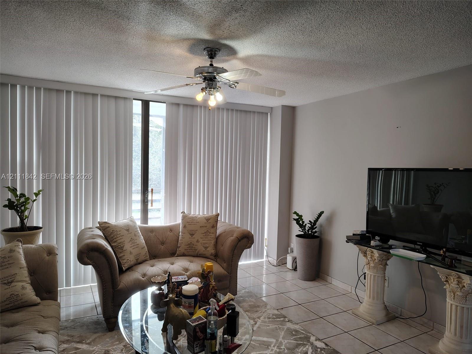 Living area featuring tile flooring, ceiling fan with integrated lighting, and floor-to-ceiling vertical blinds