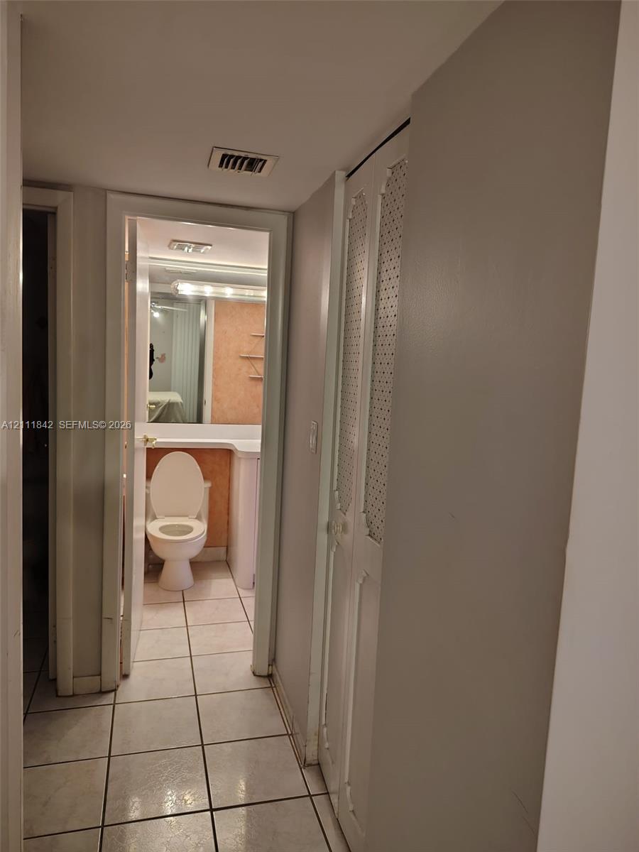 Hallway featuring light-toned ceramic tile flooring and bi-fold closet doors with decorative perforated metal panels