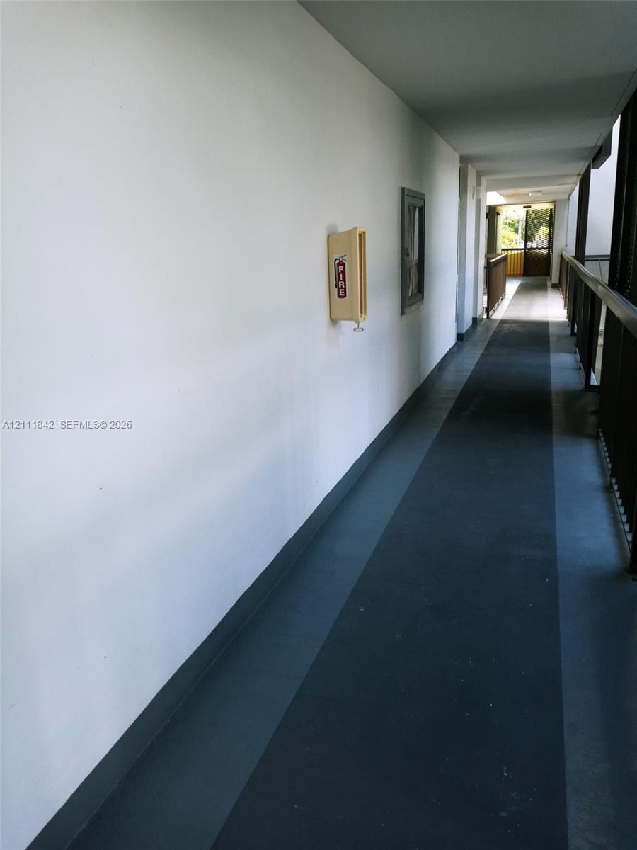 Exterior corridor featuring smooth white walls, dark-toned flooring, and a metal railing